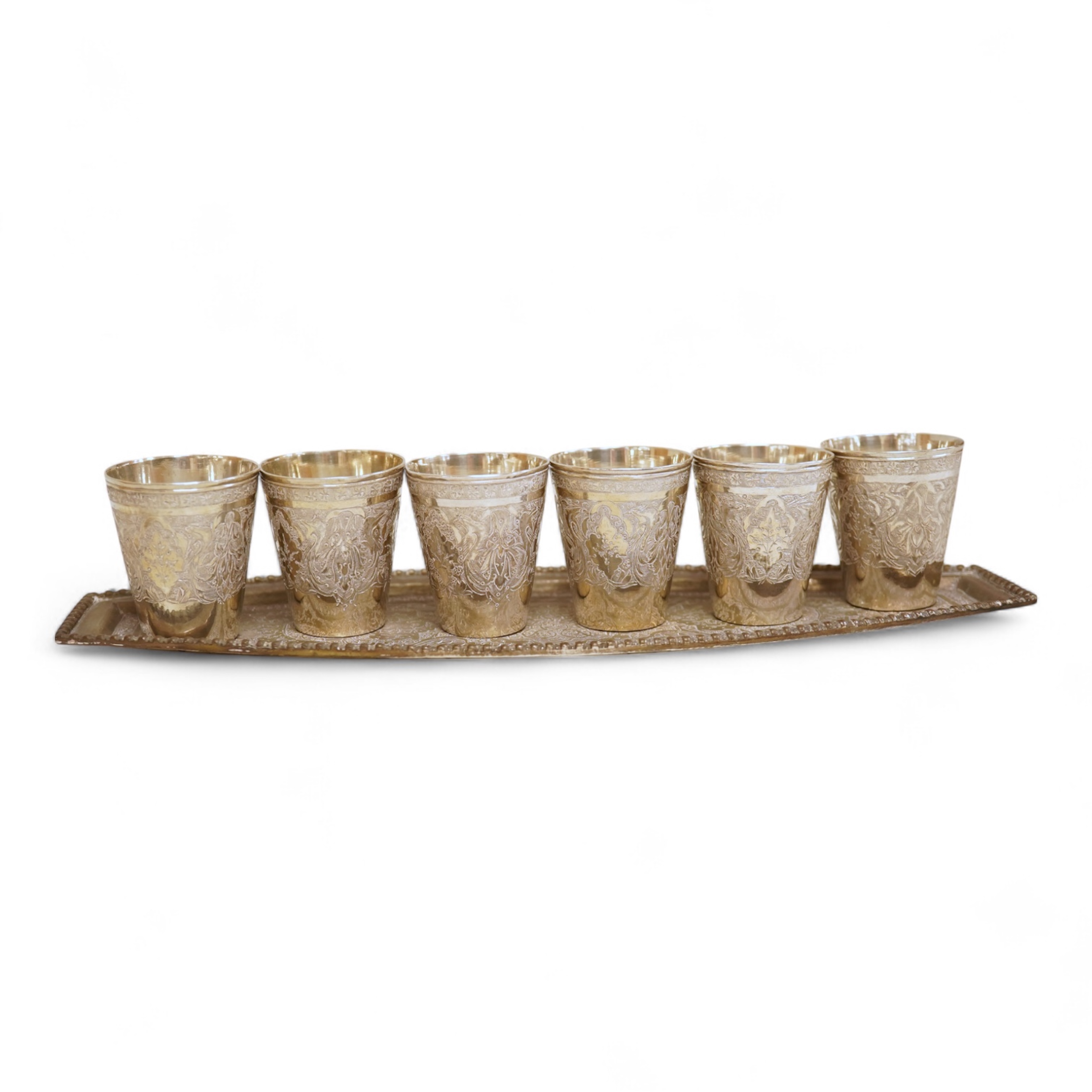 A set of six 20th century Middle Eastern white metal tots, 42mm and matching tray, 25.2cm, all engraved with geometric foliate decoration.